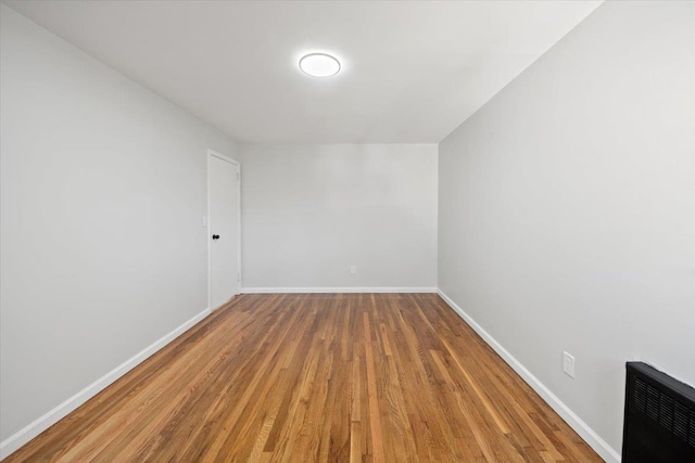 empty room featuring heating unit, wood finished floors, and baseboards