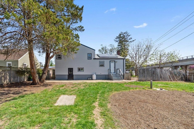 back of property featuring a lawn, a chimney, solar panels, and a fenced backyard