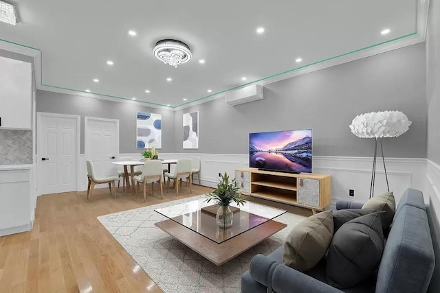 living room featuring crown molding, wainscoting, a wall unit AC, and light wood-type flooring