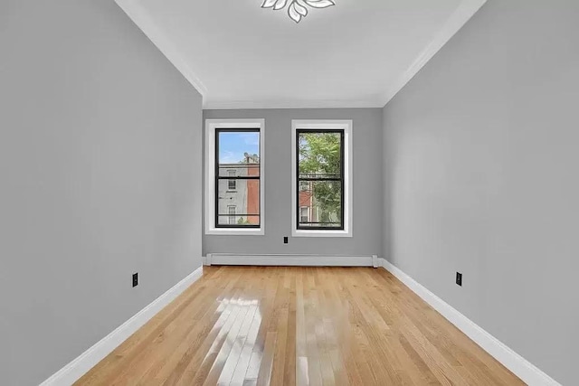 empty room featuring light wood-style floors, baseboards, crown molding, and baseboard heating
