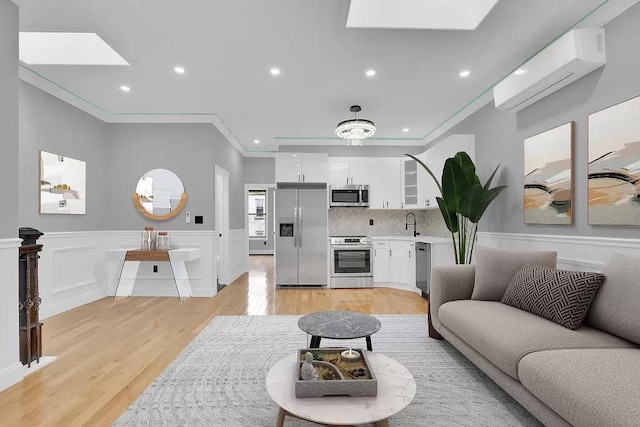living room featuring a skylight, crown molding, wainscoting, an AC wall unit, and light wood-style floors