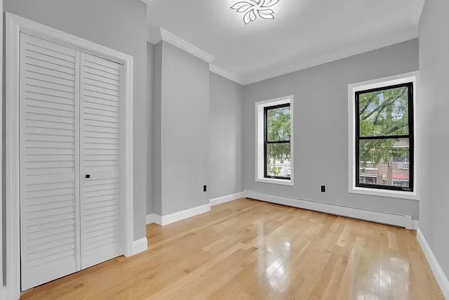 unfurnished bedroom featuring crown molding, a closet, baseboards, a baseboard heating unit, and light wood-style flooring
