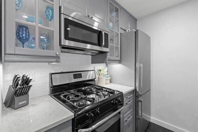 377 Westchester Ave Unit 6C, Port Chester, NY 10573 - kitchen with appliances with stainless steel finishes, gray cabinetry, tasteful backsplash, glass insert cabinets, and light stone countertops