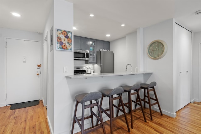 377 Westchester Ave Unit 6C, Port Chester, NY 10573 - kitchen featuring stainless steel appliances, gray cabinets, a kitchen breakfast bar, light countertops, and light wood finished floors