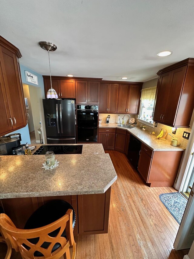 33 41st St, Islip, NY 11751 - kitchen featuring hanging light fixtures, a sink, light wood finished floors, a peninsula, and black appliances