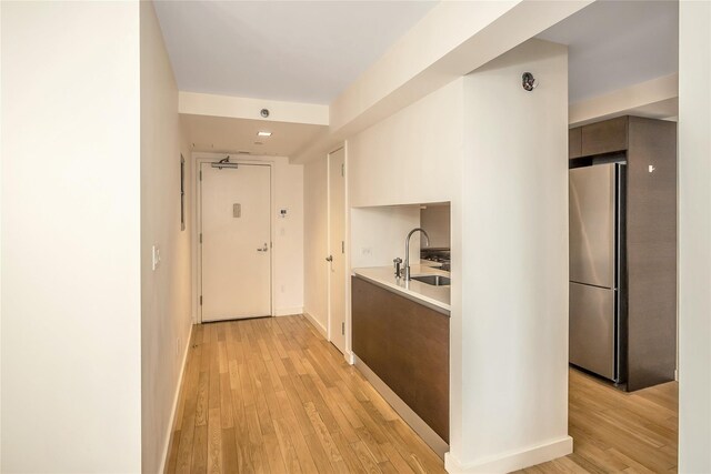 hallway with a sink, baseboards, and light wood-style floors
