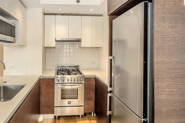 kitchen featuring backsplash, appliances with stainless steel finishes, a sink, light countertops, and white cabinetry
