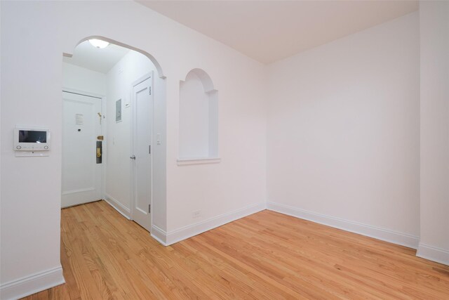 empty room with light wood finished floors, arched walkways, and baseboards