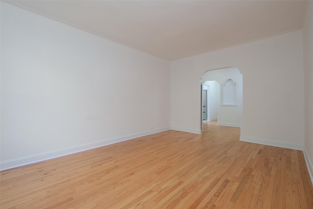 spare room featuring arched walkways, baseboards, ornamental molding, and light wood-type flooring