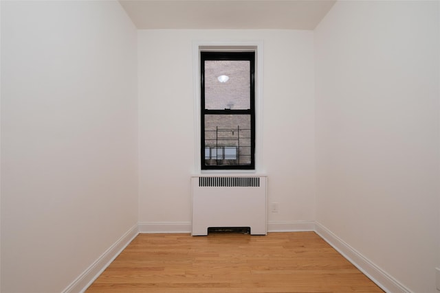 spare room with baseboards, radiator, and light wood-style floors
