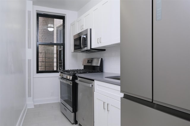 kitchen with dark countertops, stainless steel appliances, white cabinetry, baseboards, and tasteful backsplash
