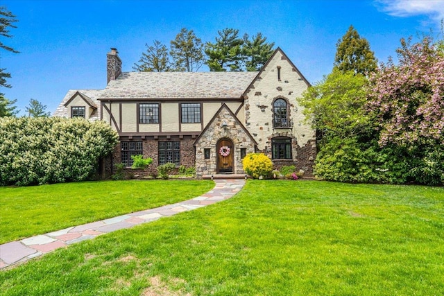 english style home with a chimney, a front yard, and stone siding