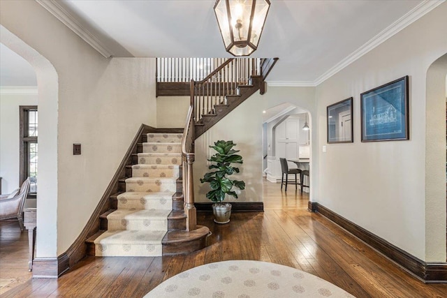 entryway featuring baseboards, stairs, crown molding, arched walkways, and hardwood / wood-style floors