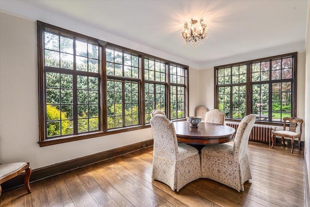 dining space featuring wood-type flooring, a notable chandelier, baseboards, and radiator heating unit