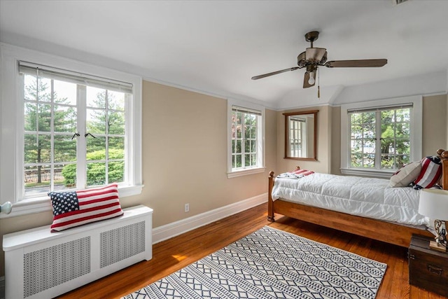 bedroom with baseboards, radiator, multiple windows, and wood finished floors