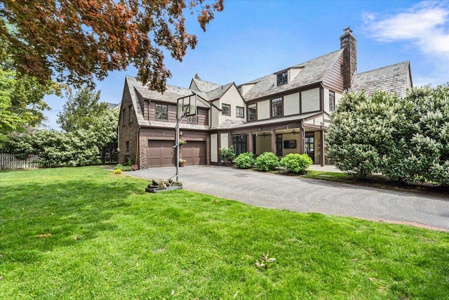 english style home featuring aphalt driveway, fence, a high end roof, a garage, and a front lawn