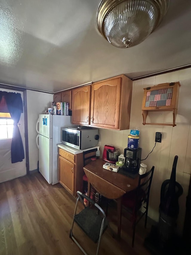 kitchen featuring stainless steel microwave, wood finished floors, brown cabinets, freestanding refrigerator, and light countertops