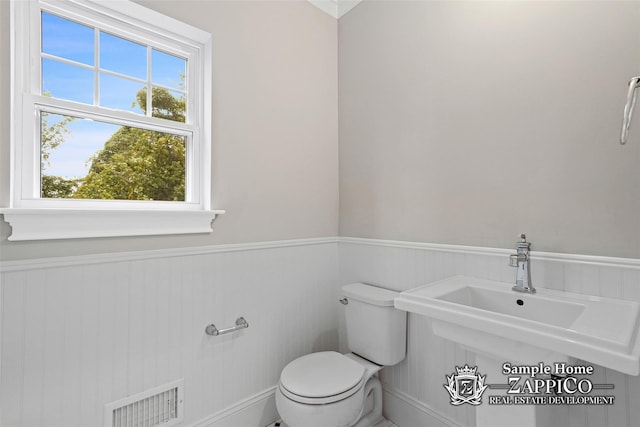 bathroom featuring wainscoting, toilet, a sink, and visible vents