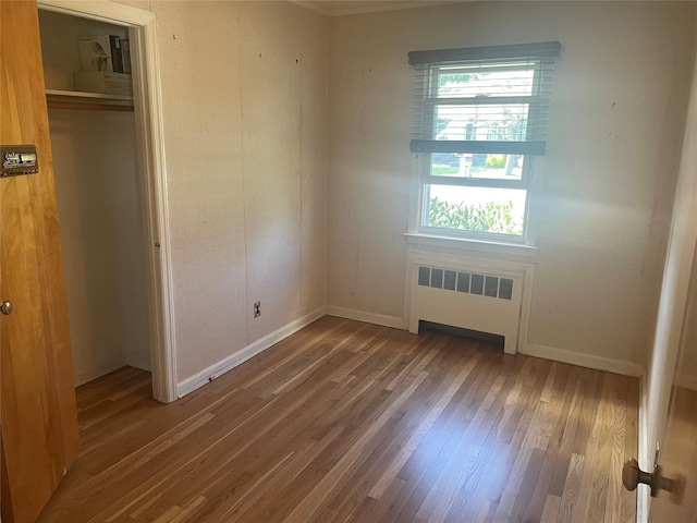 unfurnished bedroom featuring radiator, wood finished floors, a closet, and baseboards