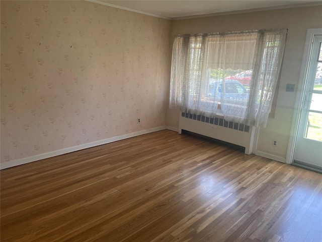 spare room featuring radiator, wood finished floors, wallpapered walls, crown molding, and baseboards