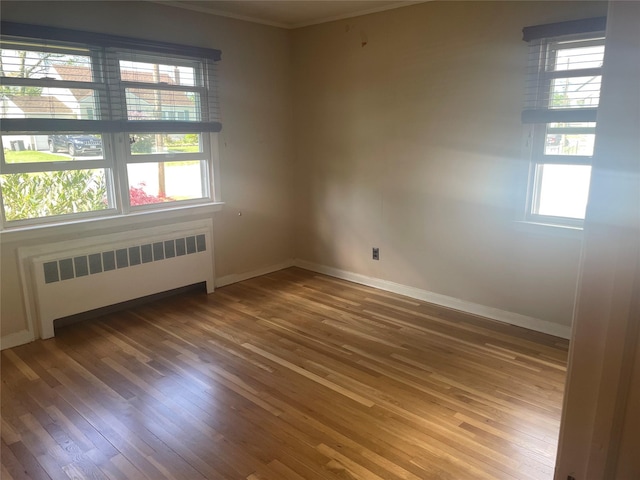 empty room with radiator, wood finished floors, ornamental molding, and baseboards