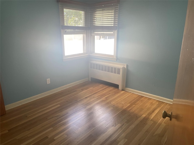 empty room featuring radiator, wood finished floors, and baseboards