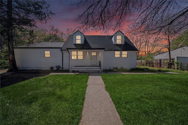 cape cod-style house with fence, covered porch, a yard, and roof with shingles
