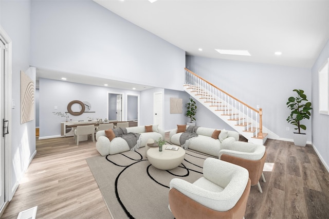 living room featuring stairway, high vaulted ceiling, light wood-style floors, and visible vents