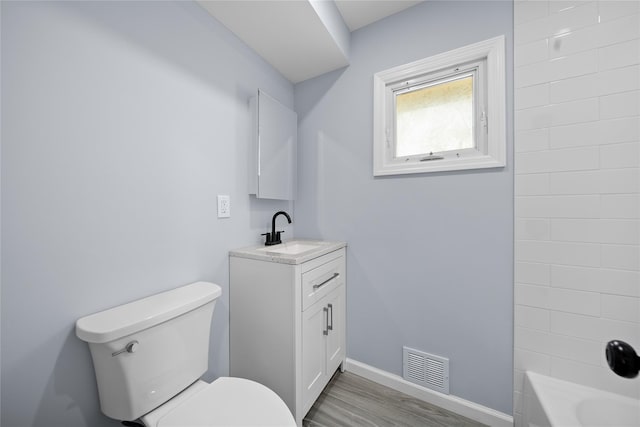 bathroom featuring vanity, toilet, baseboards, wood finished floors, and visible vents