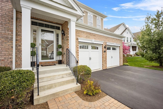view of exterior entry featuring an attached garage, stone siding, and aphalt driveway