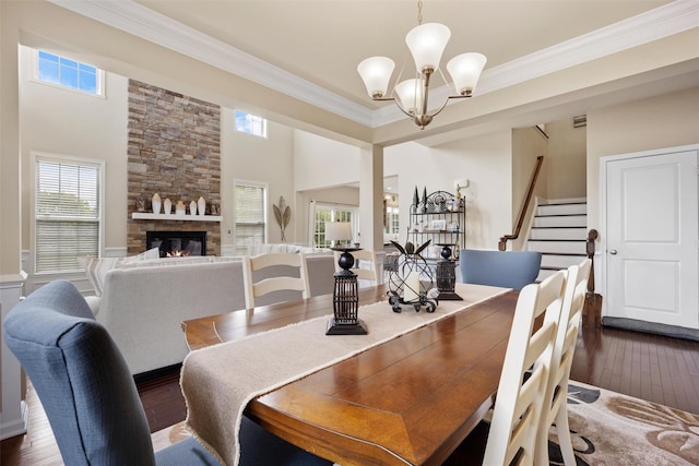dining area with an inviting chandelier, crown molding, dark wood-style flooring, stairs, and a fireplace
