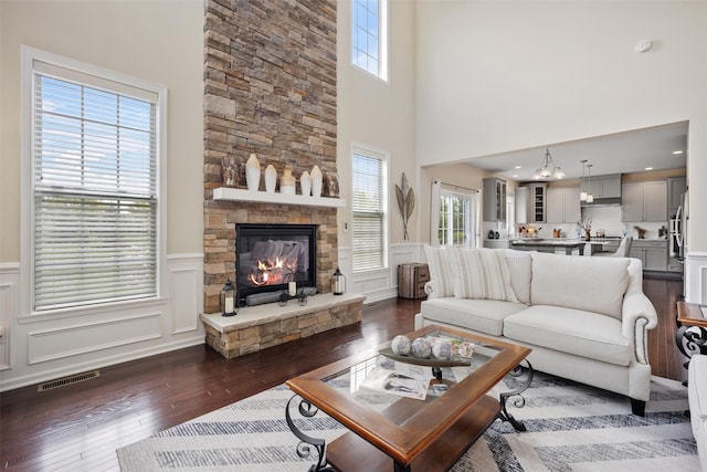 living room with plenty of natural light, dark wood-style floors, a stone fireplace, and visible vents