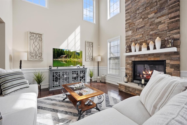 living room with wainscoting, a high ceiling, a stone fireplace, and wood finished floors