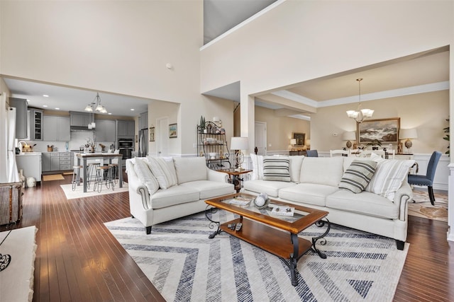 living area with an inviting chandelier, crown molding, a high ceiling, and dark wood-type flooring