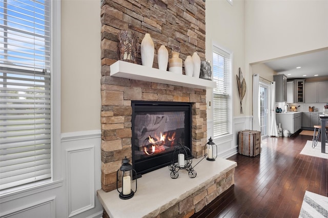 living area featuring a stone fireplace, wainscoting, dark wood-style flooring, and a towering ceiling