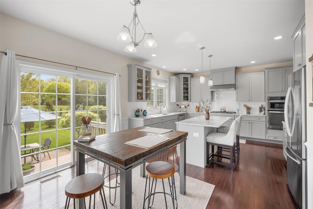 kitchen featuring glass insert cabinets, a center island, gray cabinets, a sink, and appliances with stainless steel finishes
