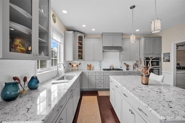 kitchen featuring light stone counters, a sink, gray cabinets, a center island, and stainless steel appliances