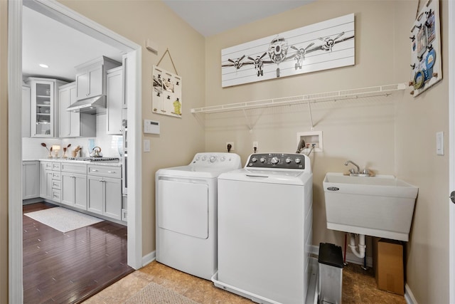 laundry area with laundry area, wood finished floors, a sink, baseboards, and washer and dryer