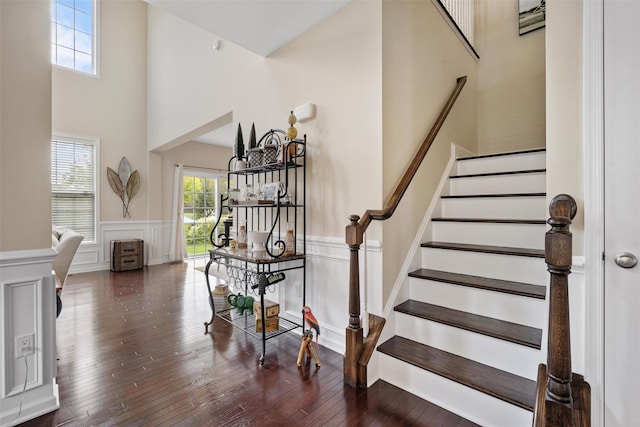 staircase featuring wood-type flooring, a decorative wall, wainscoting, and a towering ceiling
