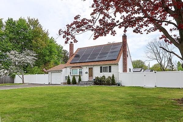 cape cod-style house featuring a chimney, a garage, fence, roof mounted solar panels, and a front lawn