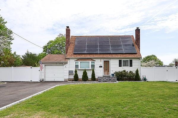 cape cod house with an attached garage, a chimney, solar panels, and aphalt driveway