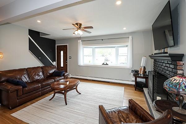 living room featuring baseboard heating, a brick fireplace, a ceiling fan, recessed lighting, and wood finished floors