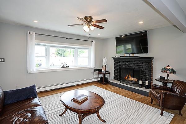 living room with ceiling fan, a brick fireplace, wood finished floors, a baseboard heating unit, and recessed lighting