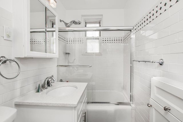 full bath with tile walls, toilet, vanity, and combined bath / shower with glass door