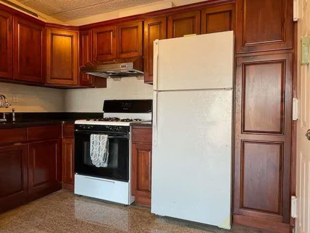 kitchen featuring dark countertops, under cabinet range hood, and white appliances