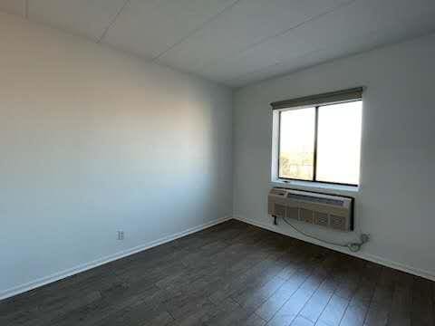 spare room with dark wood-type flooring, baseboards, and a wall unit AC