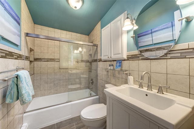 bathroom featuring tile walls, toilet, enclosed tub / shower combo, and vanity