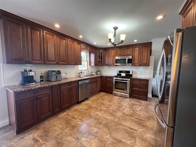 kitchen with a notable chandelier, light stone counters, a sink, stainless steel appliances, and decorative backsplash