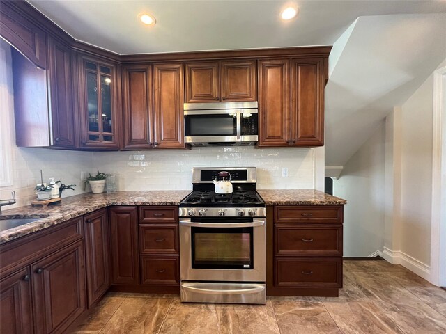 kitchen featuring decorative backsplash, light stone countertops, a sink, glass insert cabinets, and stainless steel appliances