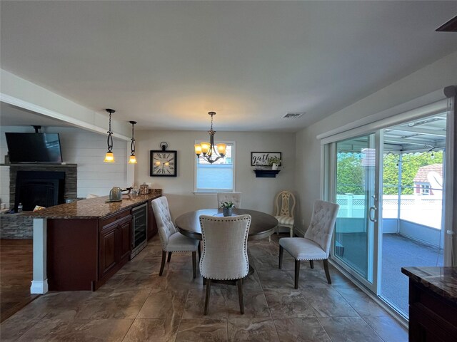 dining area featuring stone finish flooring, visible vents, a fireplace with raised hearth, beverage cooler, and an inviting chandelier